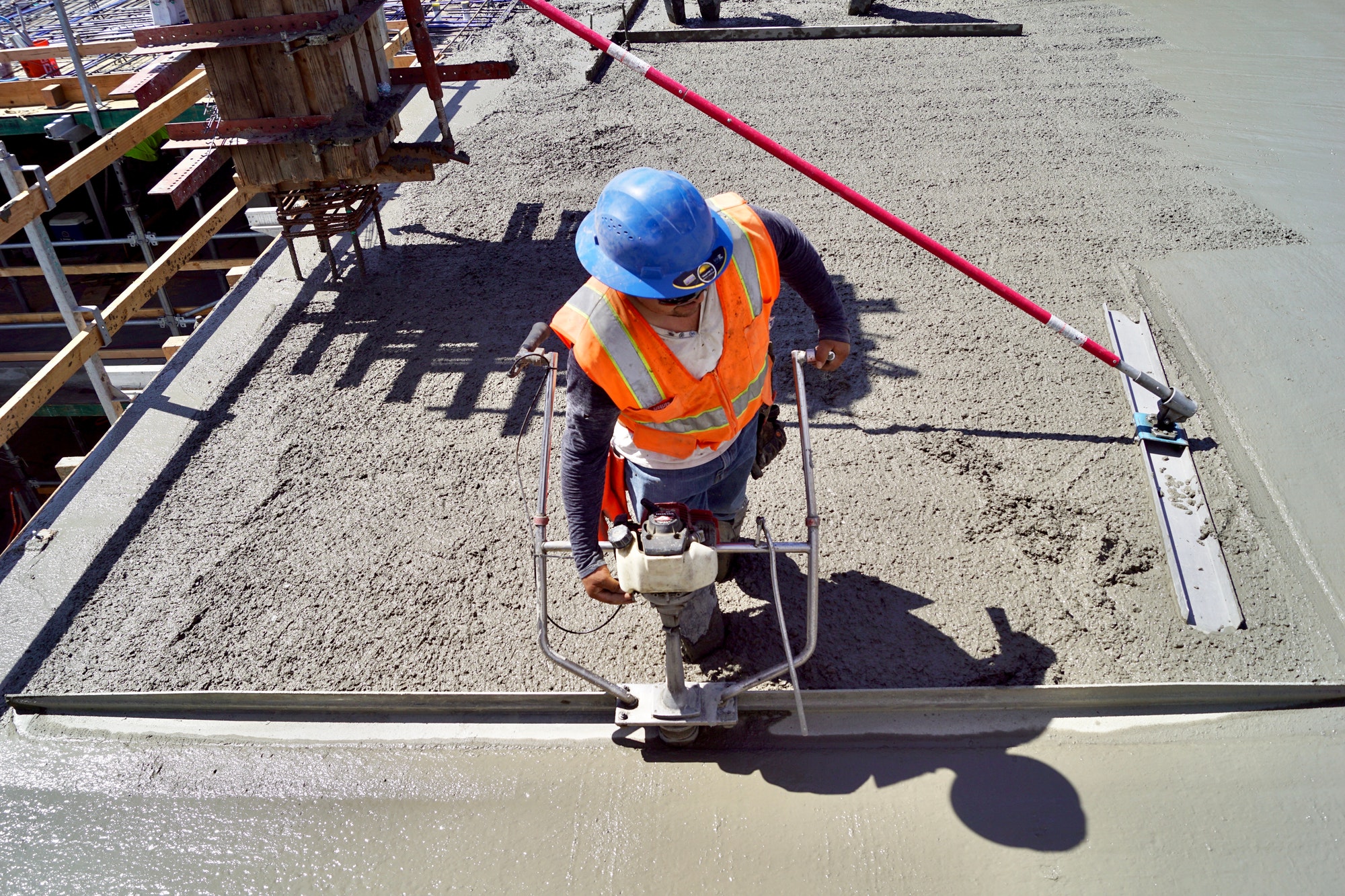 A construction worker is standing knee deep in wet cement while he is leveling a different plane of